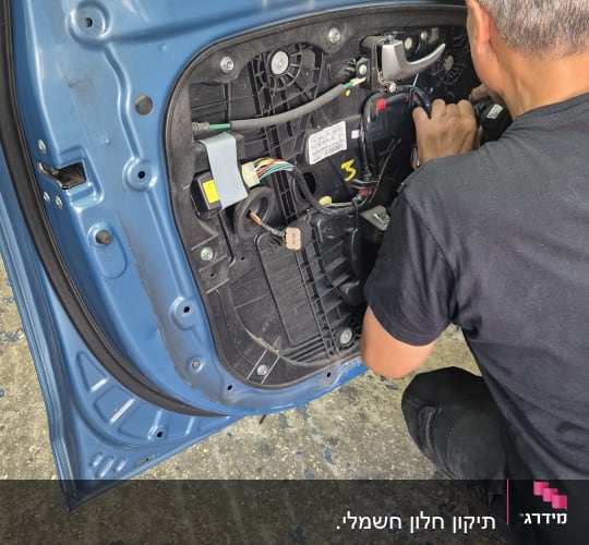 אדם עובד על דלת רכב בסדנה עם כלים וחוטים